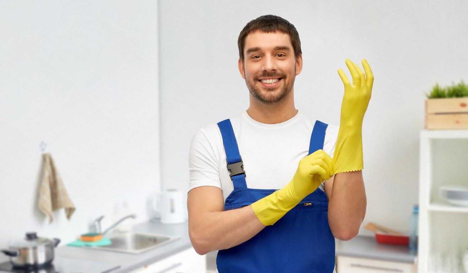 Plumber in blue overalls putting on yellow gloves before a kitchen plumbing repair