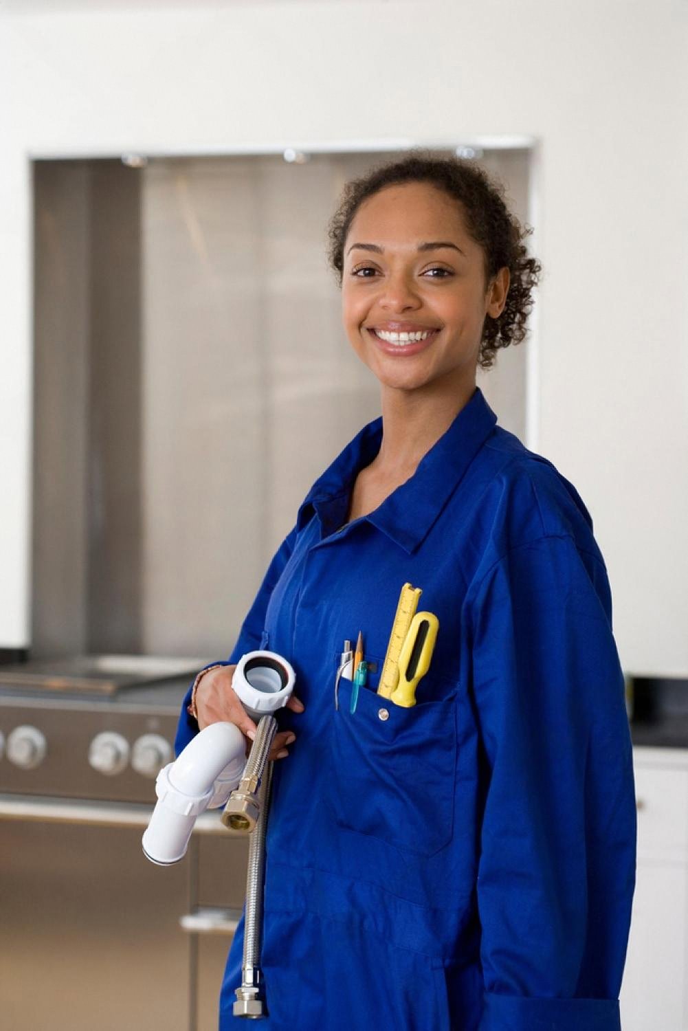 Uniformed plumber holding a sink trap and flexible hose inside a UAE apartment kitchen